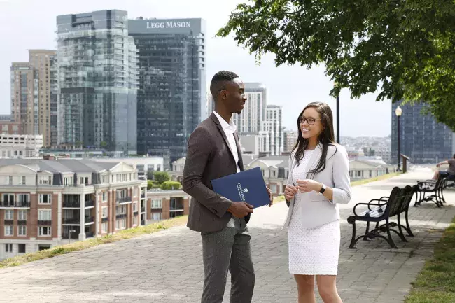 two students outside Carey the walkway overlooking the Baltimore skyline discussing Carey programs