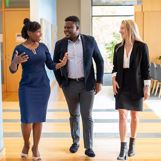 A diverse trio of adults appear to walk toward the camera, talking and smiling at each other