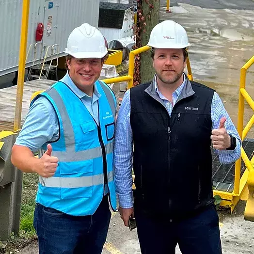 Andrew Posil and Michael Hutton wearing hard hats and with thumbs up in a warehouse