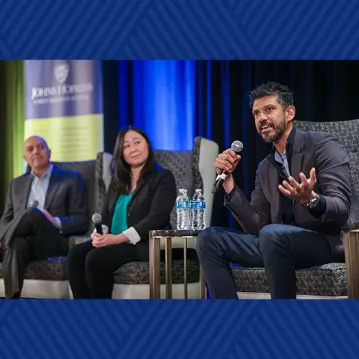 three people seated on a stage as a panel with Dean Triantis, and AstraZeneca executives