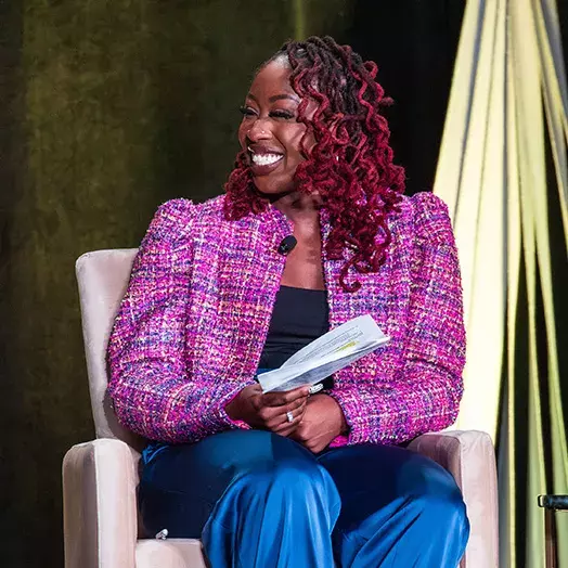 MoAndra Johnson sitting on stage smiling and holding paper notes.