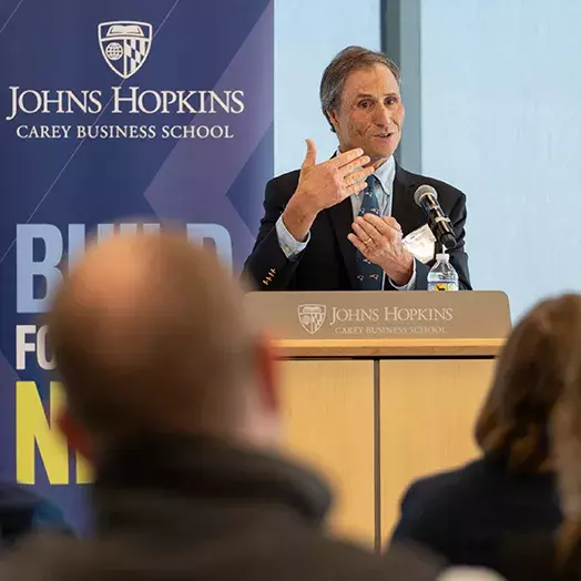 Godes at the podium with JHU Carey Business School banner