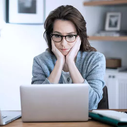 Hook article woman contemplating a laptop in her office with hands propping up her face.