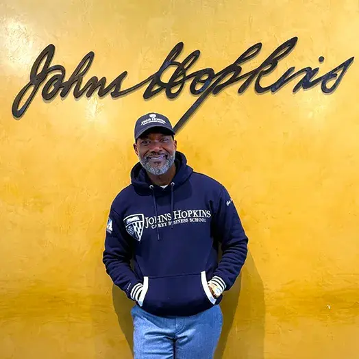 man standing against orange wall with johns hopkins sign above