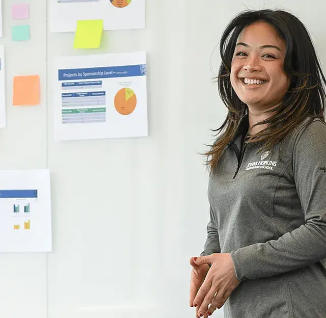 Student smiling while presenting data charts on a wall