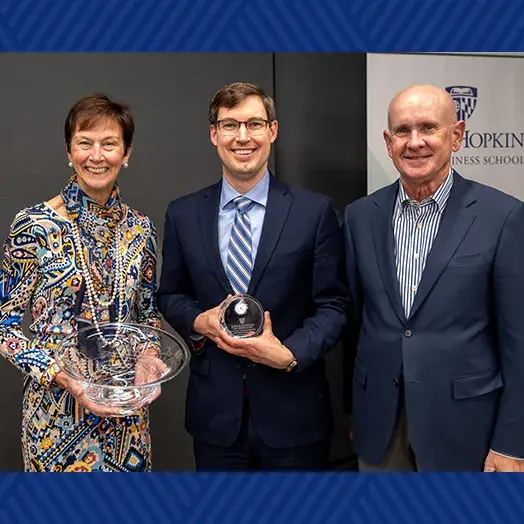 Christopher Myers (center), inaugural Peetz Family Professor of Leadership, accepting an award from Karen Peetz (left), with a male attendee/speaker at the installation event (right).
