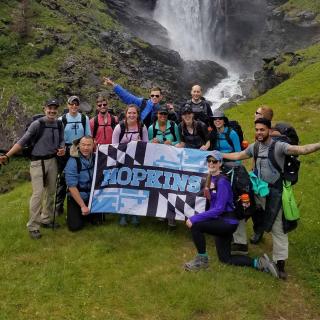 group of Hopkins student on a hike with a waterfall in the background and a Hopkins banner 