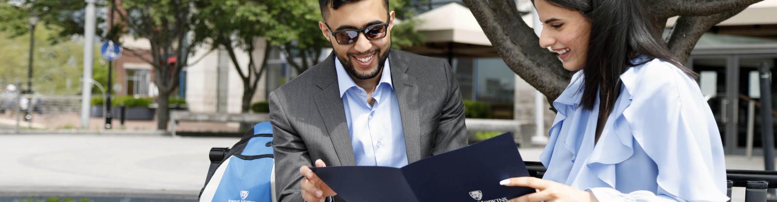 two students look down at a johns hopkins carey business school folder