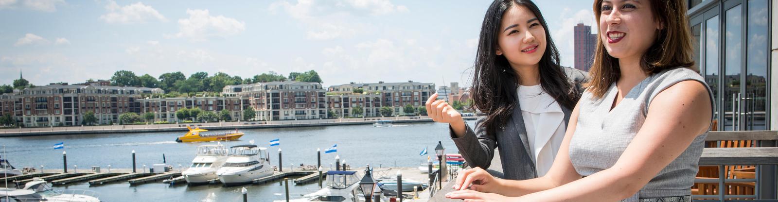two student talking and looking out over the harbor from a balcony at JHU Carey Business School