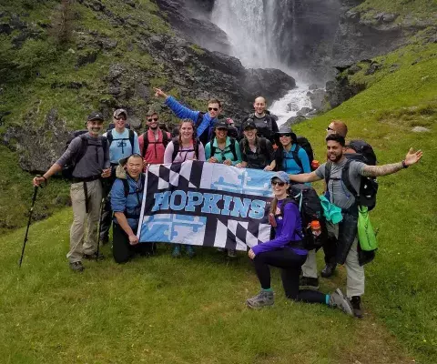 group of Hopkins student on a hike with a waterfall in the background and a Hopkins banner 