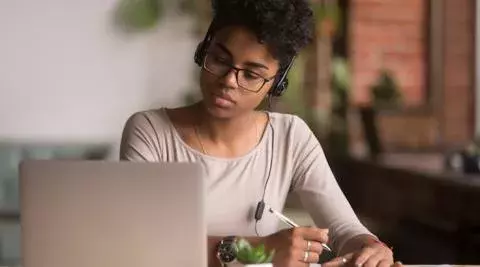 student with headphones and a pen in hand concentrating on a laptop in home setting