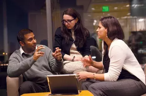 MIINT image: 3 students sitting comfortably in a lounge area at Carey business school with laptop on a small table discussing