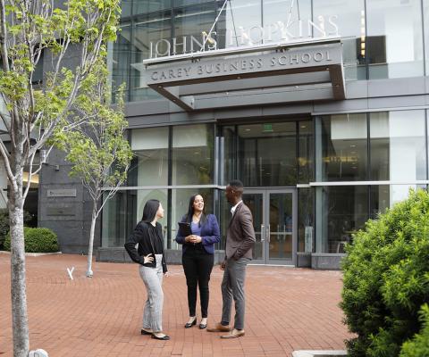 3 students on the brick plaza outside the entrance to John Hopkins Carey Business School
