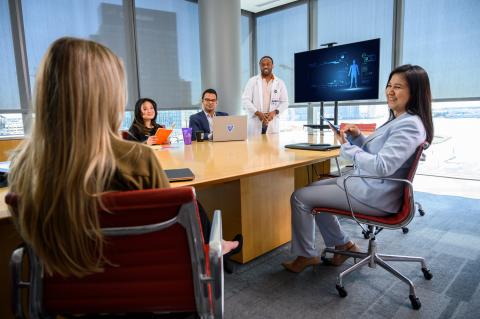 Five people in a conference room with a screen showing medical technology
