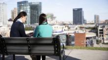 2 students sitting on a bench overlooking the city sharing a laptop