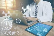 doctor in lab coat at laptop with tablet