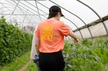 karma-farm-program-1216x800.jpg two student in a green house the one with a build for what's next t-shirt is pointing to a plant