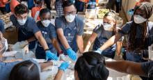 students working in a group putting hands together in the center of a table wearing surgical masks