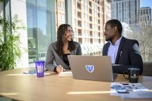 Two people at a desk staring at each other smiling