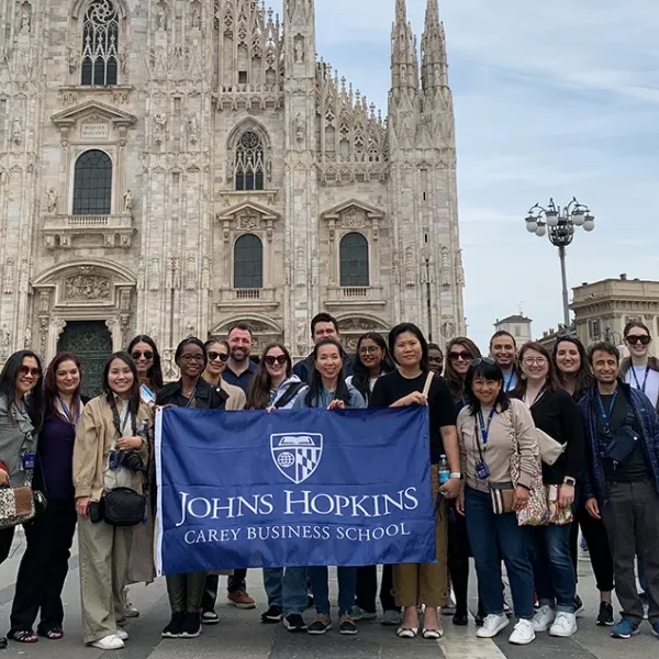 Students holding a Carey Business School flag smiling at the camera on a global immersion trip