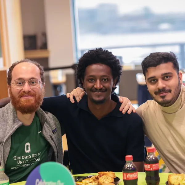 Three friends smiling at a table with food and Coca-Cola bottles indoors