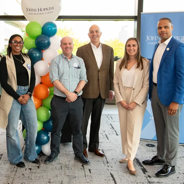 Five people posing at event beside colorful balloon column and Johns Hopkins banner