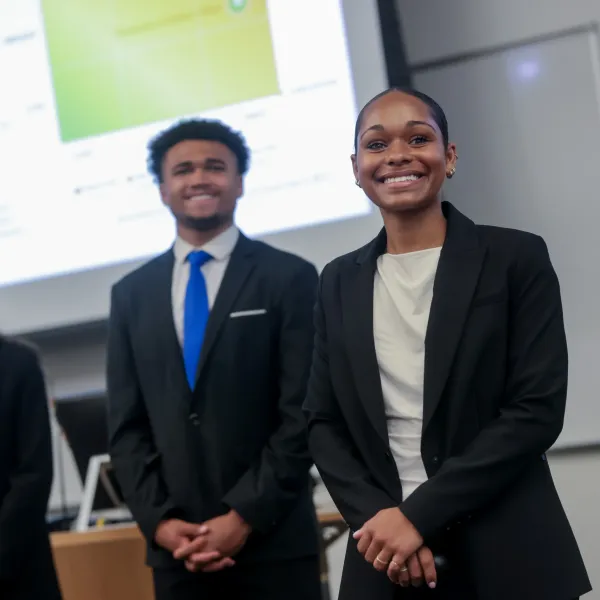 Three students smiling in front of a projected presentation slide.
