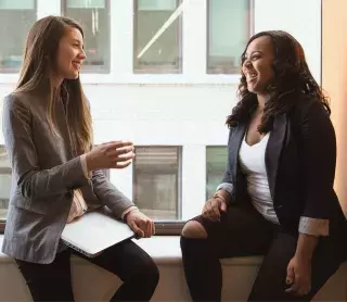 two students discussing while casually sitting on a window ledge.