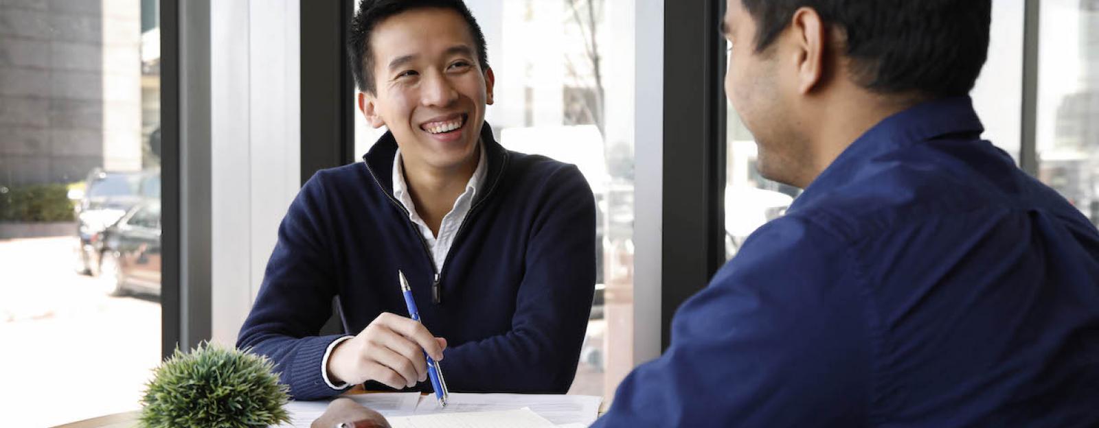 2 students inside a common area at a round table with a pland discussing a pape holding a pen