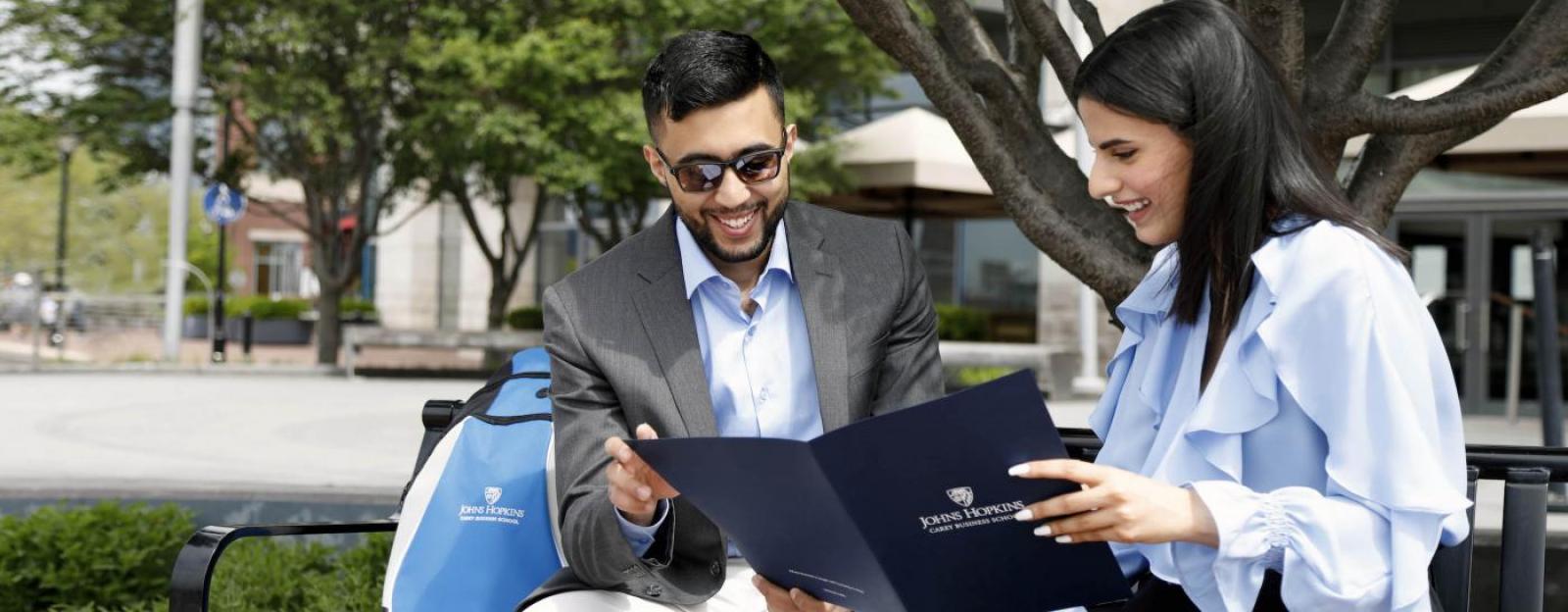 couple sharing a Carey Business School fold when siting on a campus bench