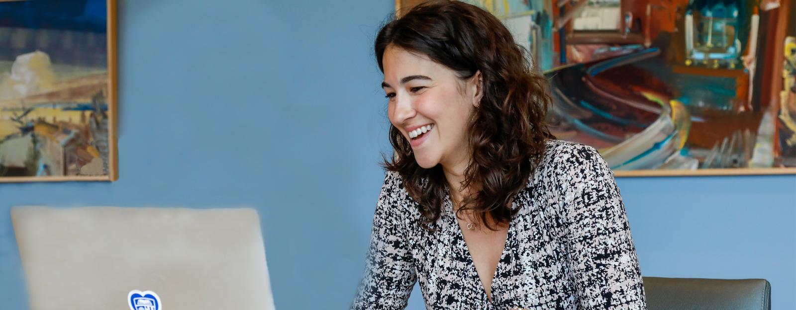 woman sitting at laptop with paintings on wall behind