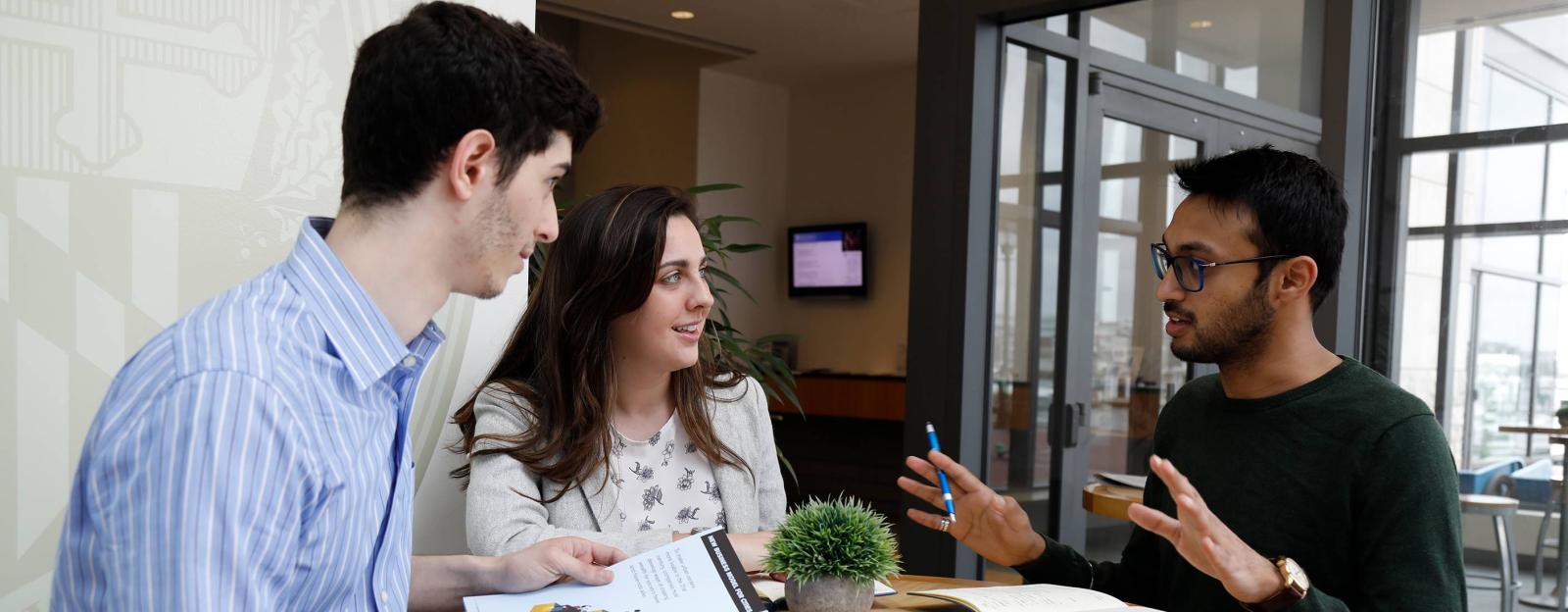3 Flex MBA students siting around a table in a campus study area discussing